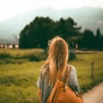 A woman with blonde hair and a backpack explores a scenic mountain landscape at sunset, capturing a sense of freedom and travel.